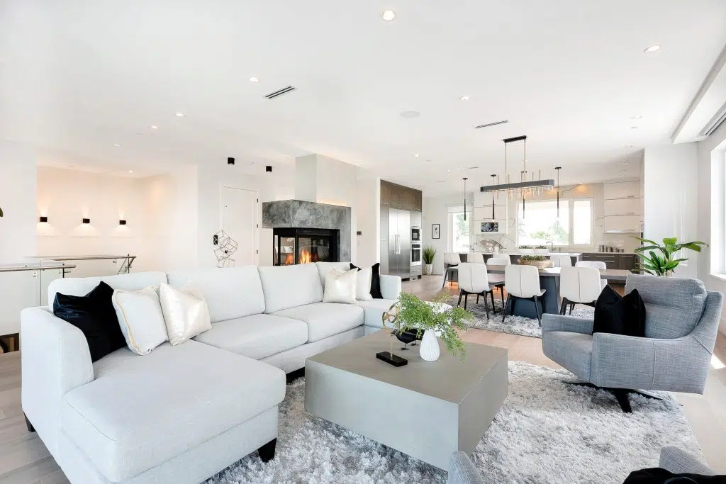 The interior of a kitchen and living area with white furnishings including a corner sofa, kitchen table, grey side table. The interior design is sleek and modern.
