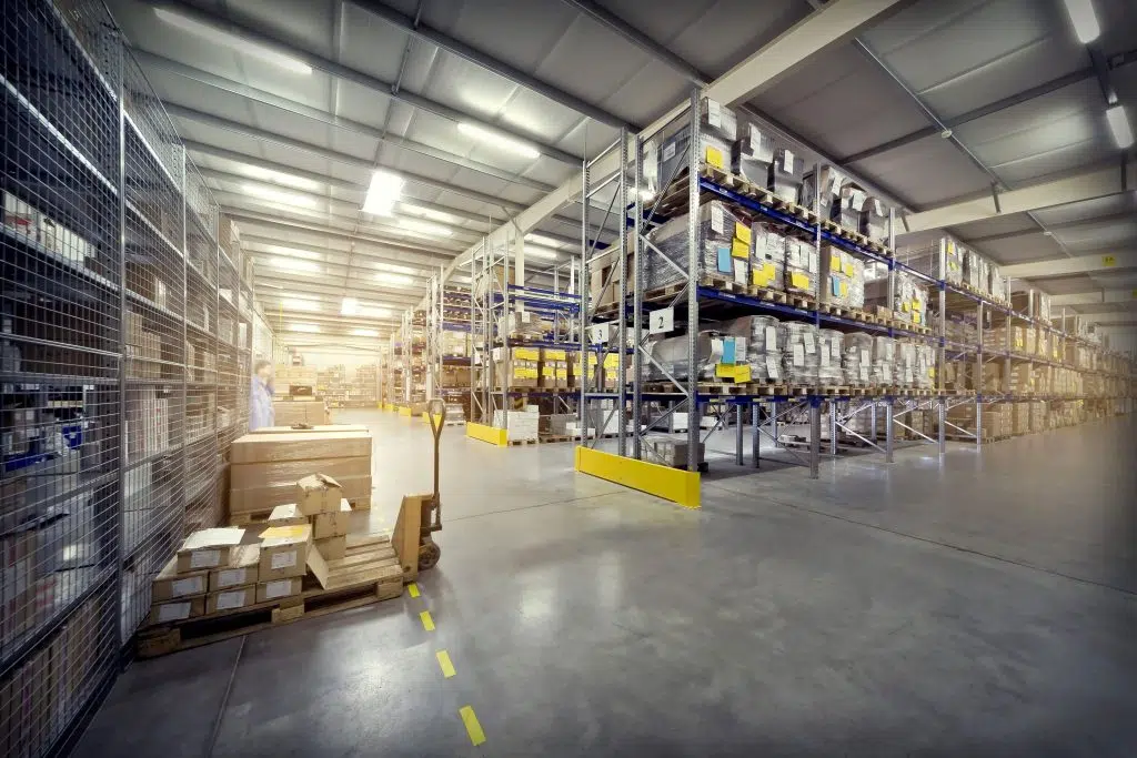 A ground floor view of a warehouse, there is lots of stock piled up on the right and there is a pallet truck on the left with stock loaded onto it