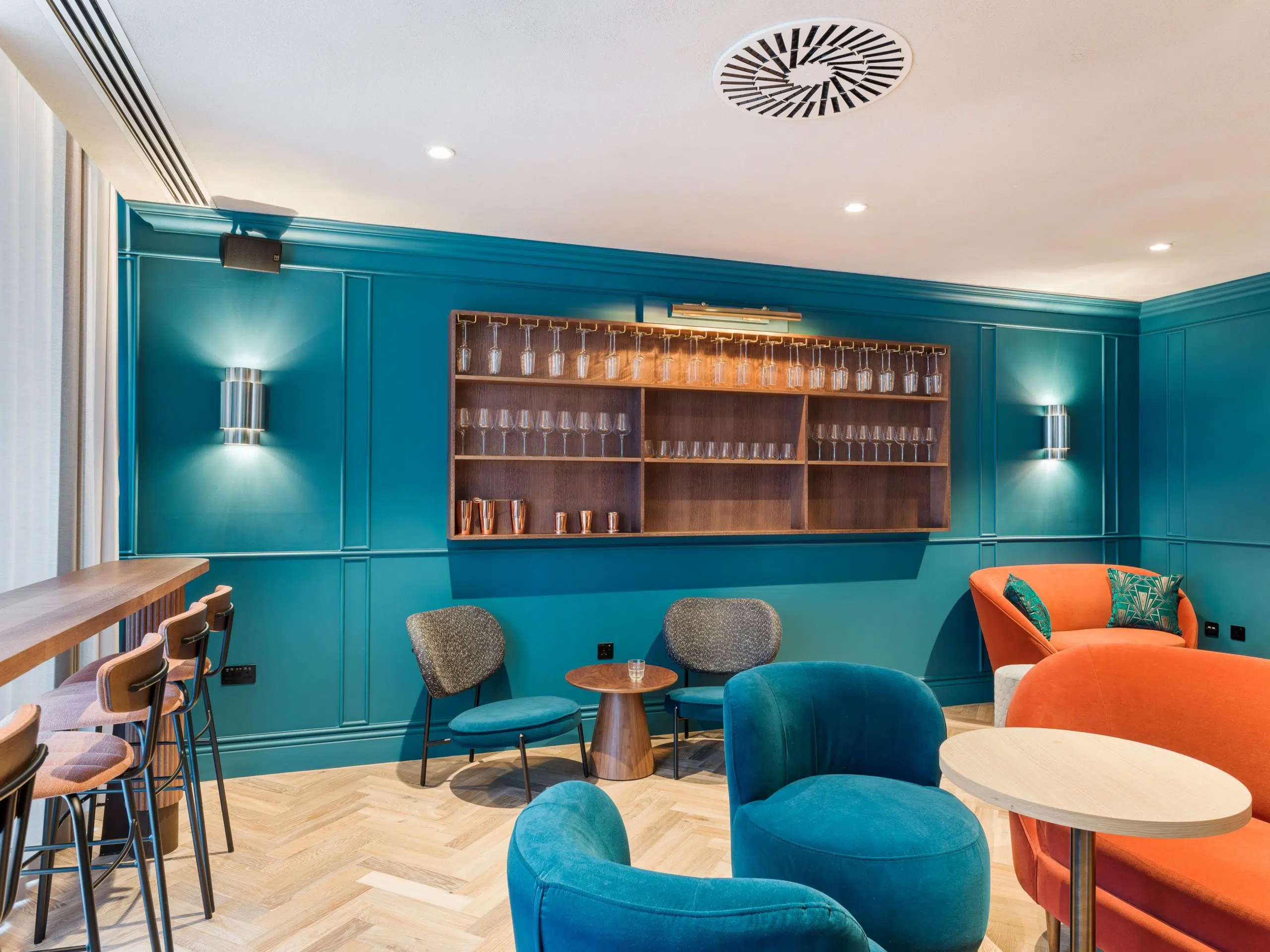a cosy office breakout area with blue walls, blue and orange arm chairs and white acoustic spray ceiling.