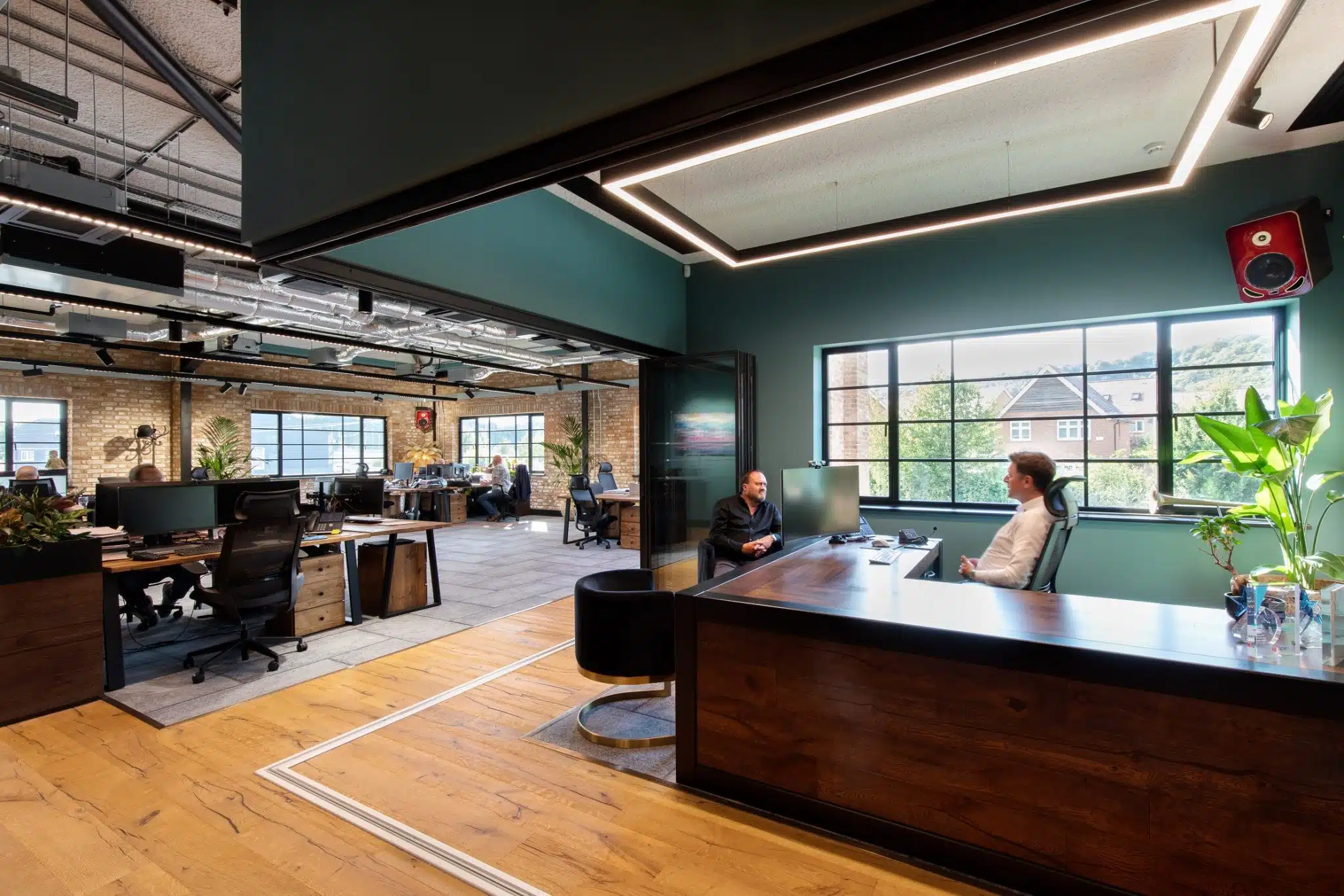 Open plan offices with interior brickwork walls and wooden floors with two people sat either side of a large wooden desk