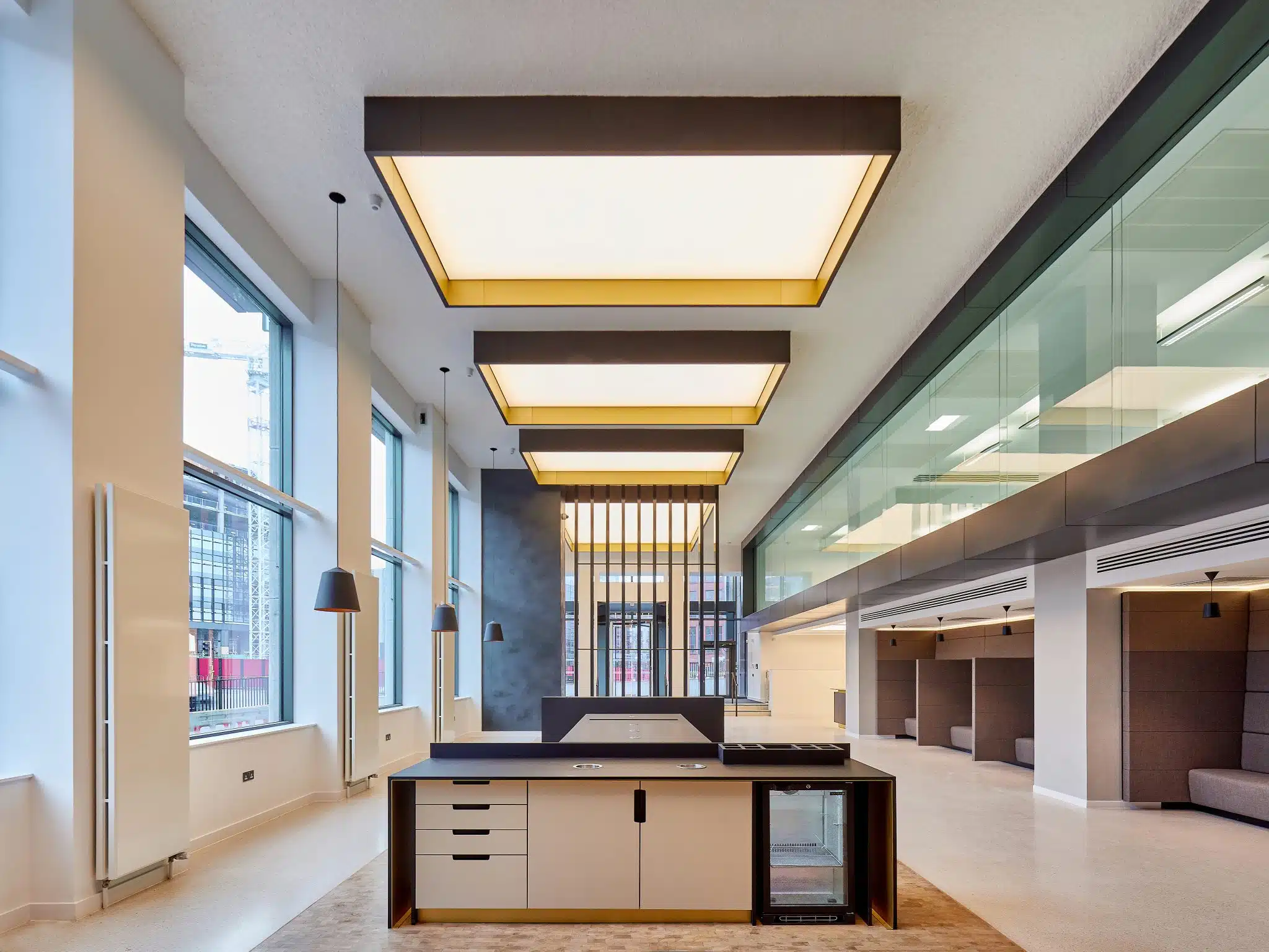 large open plan office entrance hall with stone floors, large feature lighting and brown seating booths.