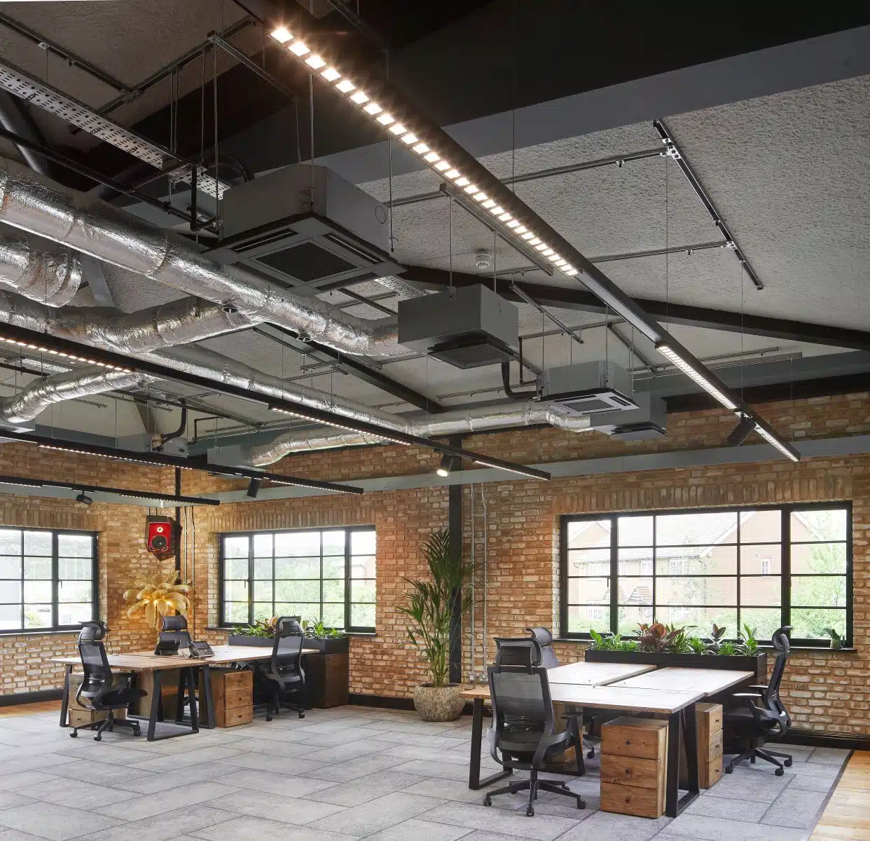 Open plan office with windows and brick work walls and acoustic spray ceiling with services.