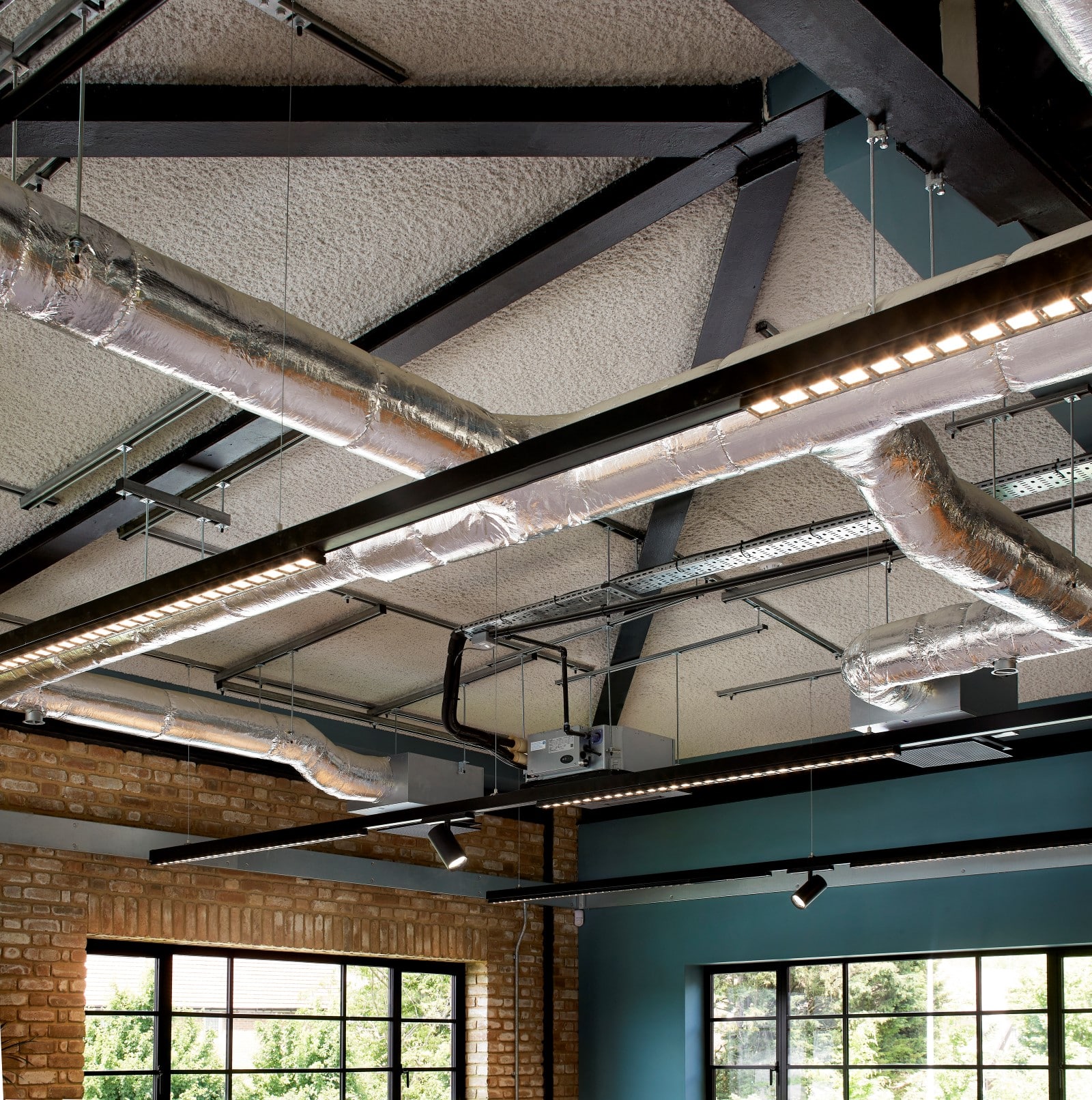 Modern office ceiling with SonaSpray k13 Special applied in light grey. Hanging lights and exposed pipes.