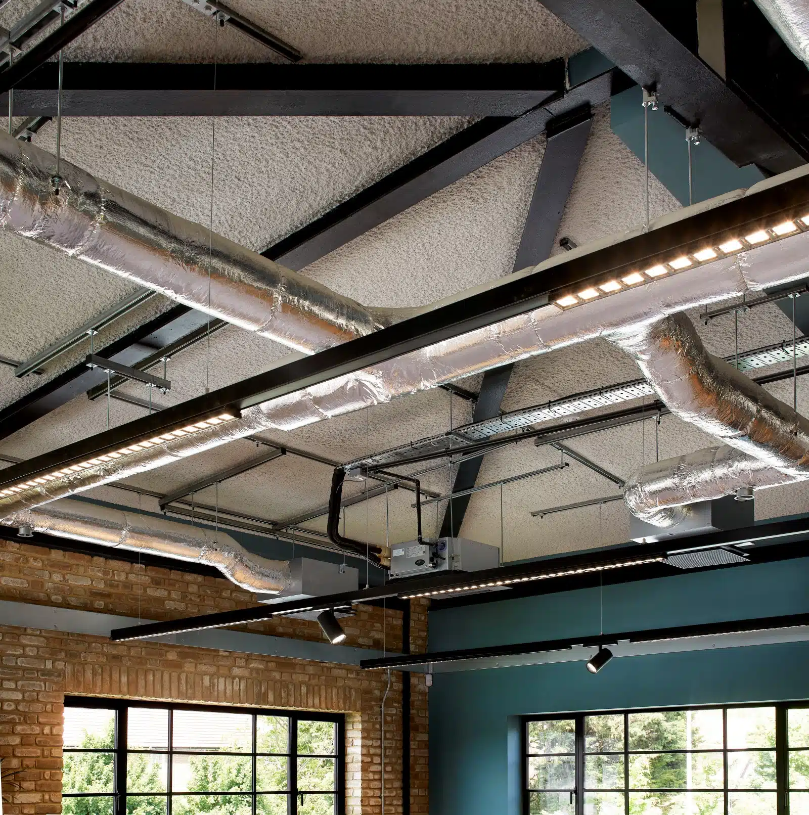 Modern office ceiling with SonaSpray k13 Special applied in light grey. Hanging lights and exposed pipes.